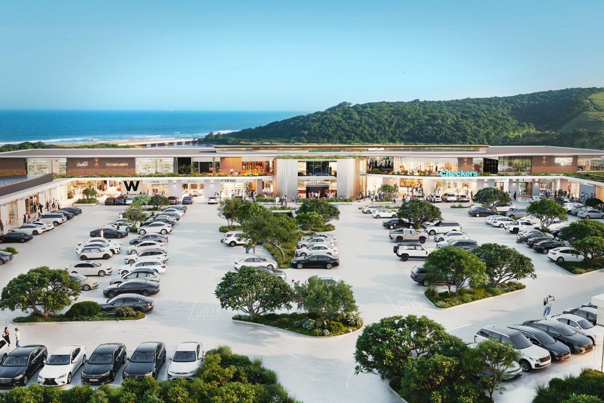 Aerial view of a modern commercial shopping center featuring extensive paved parking, landscaped areas, and prominent retail storefronts with coastal views.