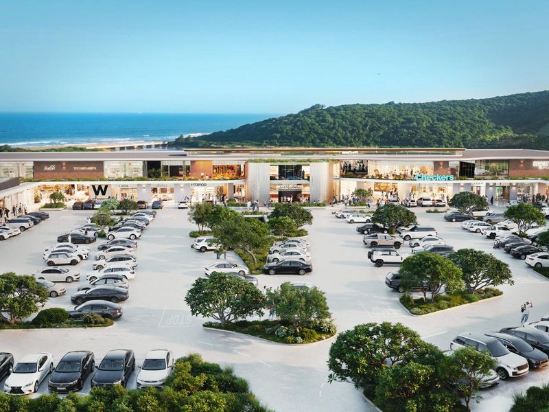 Aerial view of a modern commercial shopping center featuring extensive paved parking, landscaped areas, and prominent retail storefronts with coastal views.