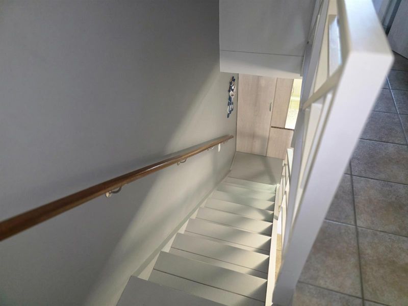 A view looking down a staircase featuring a wooden handrail and tiled flooring at the landing.