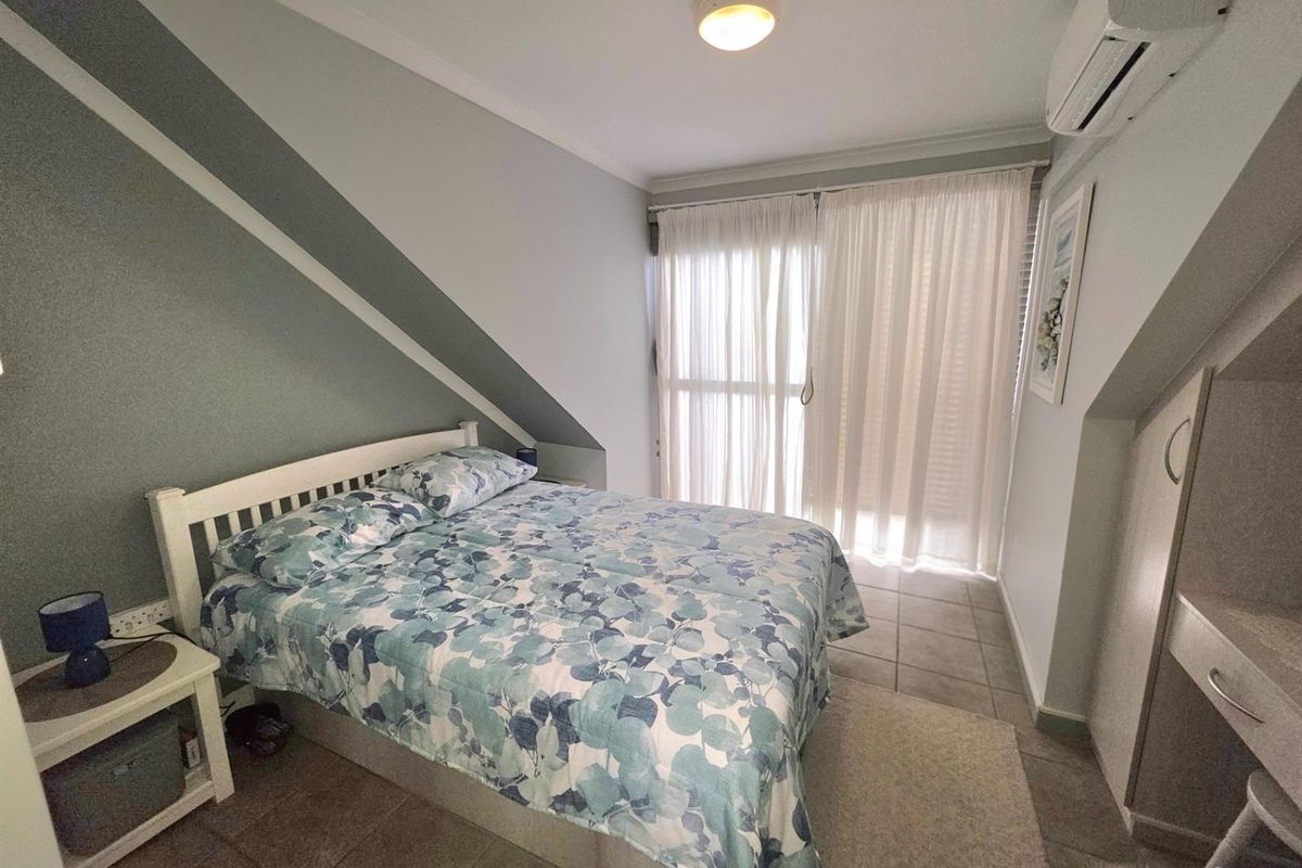 A bedroom featuring a sloped ceiling, tiled flooring, and a wall-mounted air conditioning unit, with direct access to a balcony through sliding glass doors.
