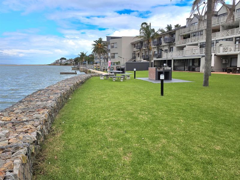 A well-maintained communal garden area featuring a stone gabion retaining wall, built-in braai facilities, and direct waterfront access.