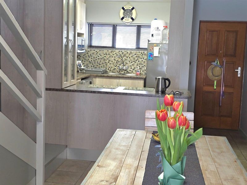 Open plan kitchen featuring a breakfast bar, mosaic tile backsplash, and neutral cabinetry, seamlessly connecting to the dining area.
