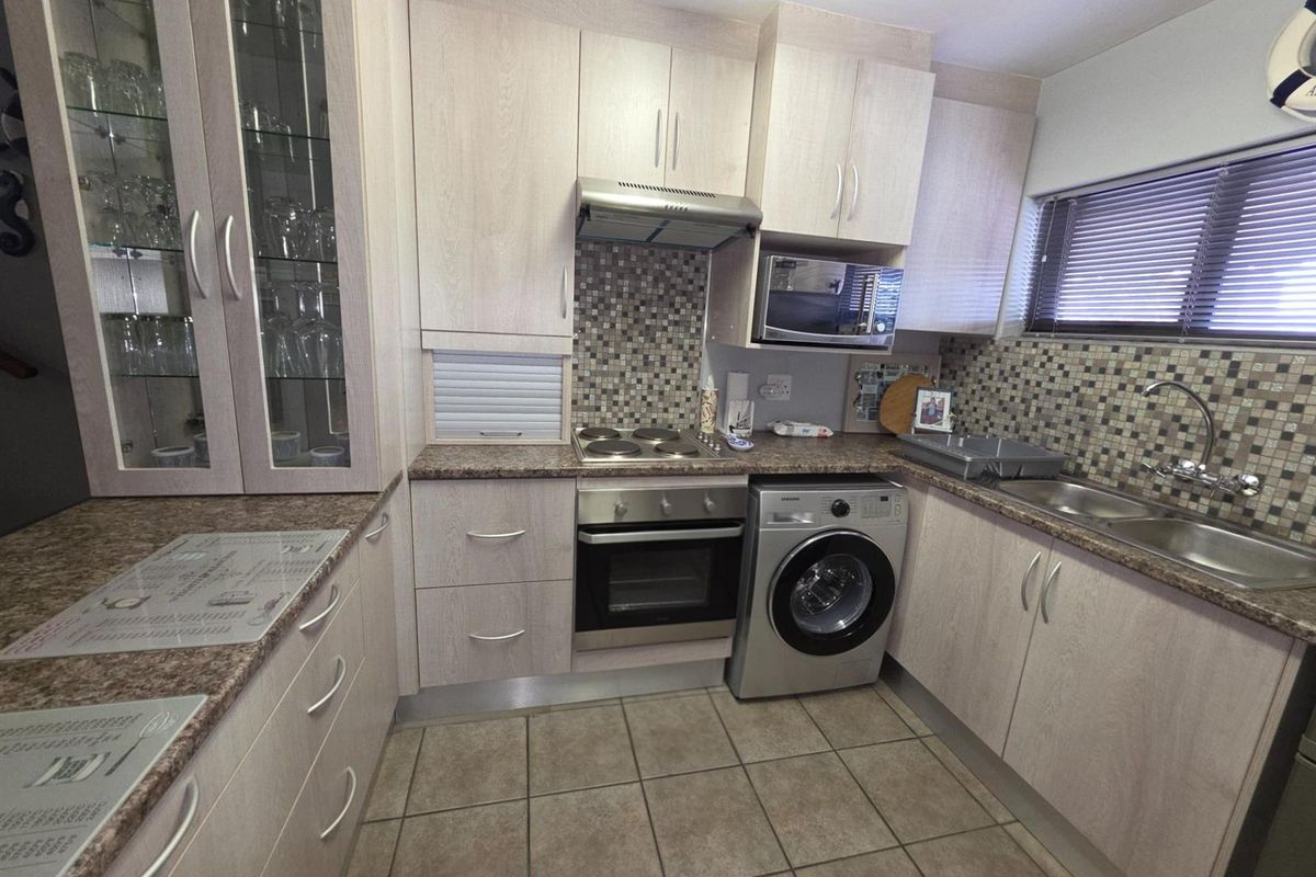 Compact kitchen featuring light wood-grain cabinetry, mosaic tile backsplash, built-in oven, electric hob, extractor fan, and integrated laundry appliance space.