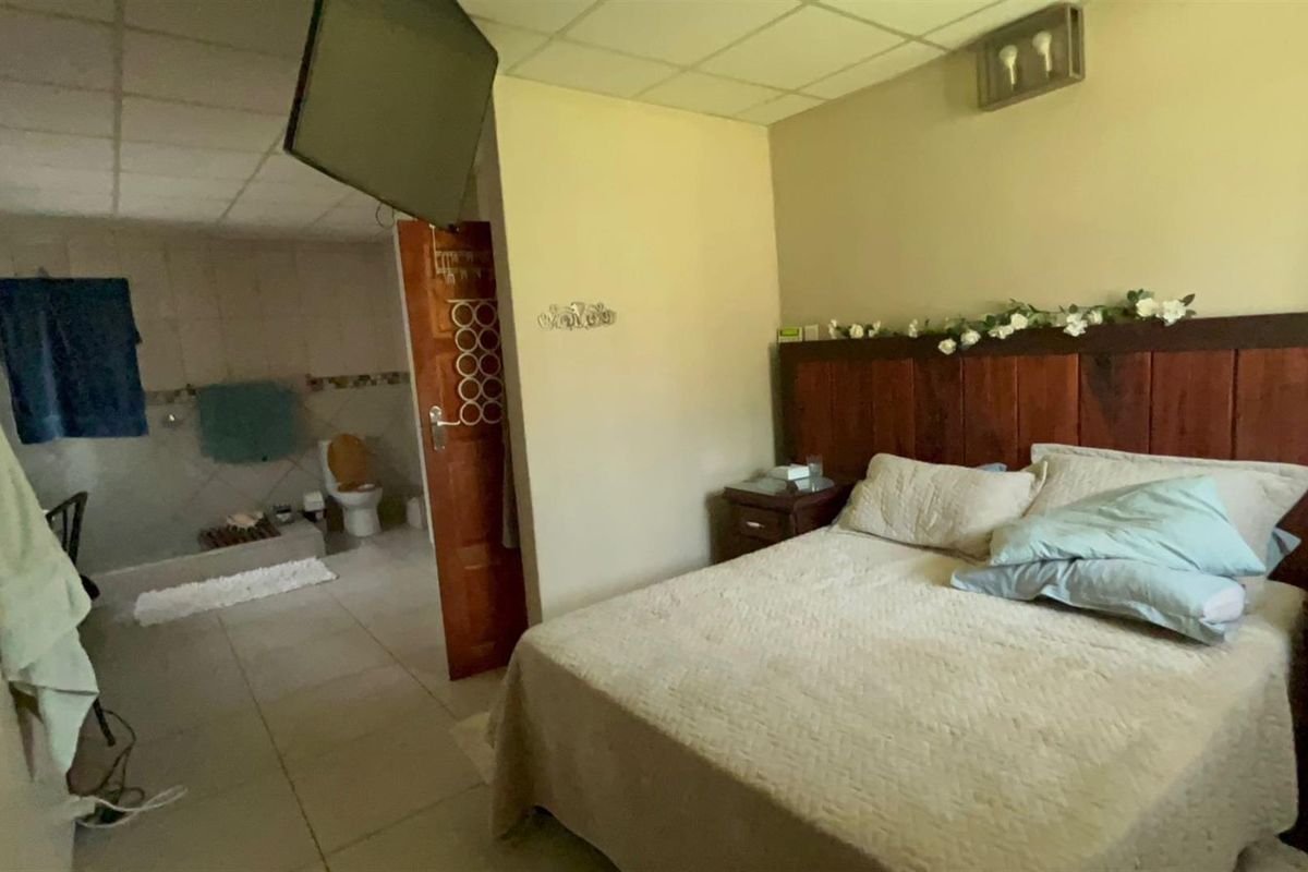 A bedroom featuring a built-in wooden headboard and an open-plan en-suite bathroom with tiled flooring.