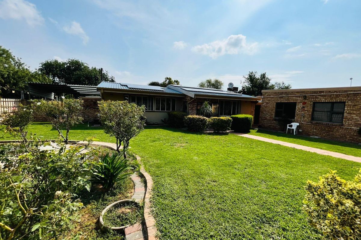 A view of the rear garden and backyard elevation of the house, featuring a well-maintained lawn, brick pathways, and established landscaping.