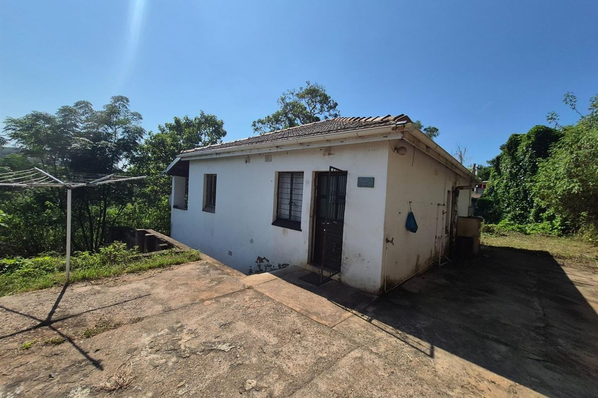 Exterior view of a detached dwelling featuring a concrete patio area, tiled roof, and security gate access.