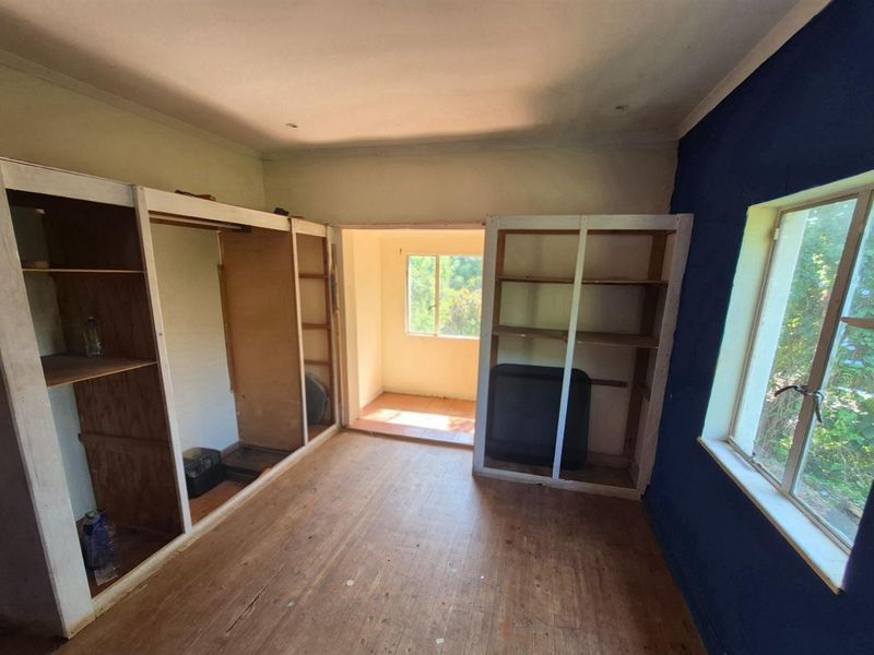 A bedroom featuring built-in timber shelving units, wooden flooring, and an adjoining sunroom area with natural light.