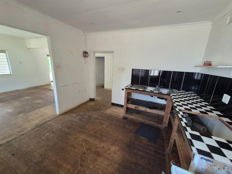 A dated kitchen area featuring tiled countertops, a double sink, and exposed timber flooring, requiring renovation and modernization.
