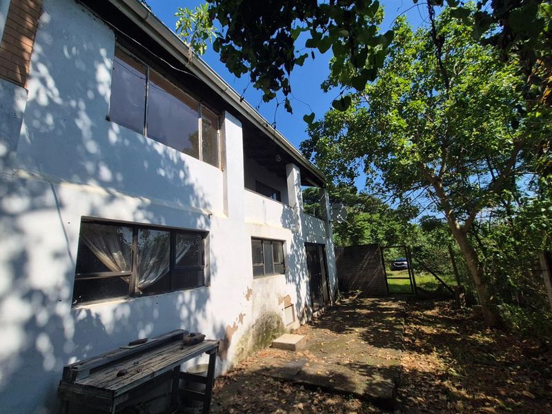 Rear exterior view of the house featuring a two-story facade, balcony, and paved patio area surrounded by mature trees.