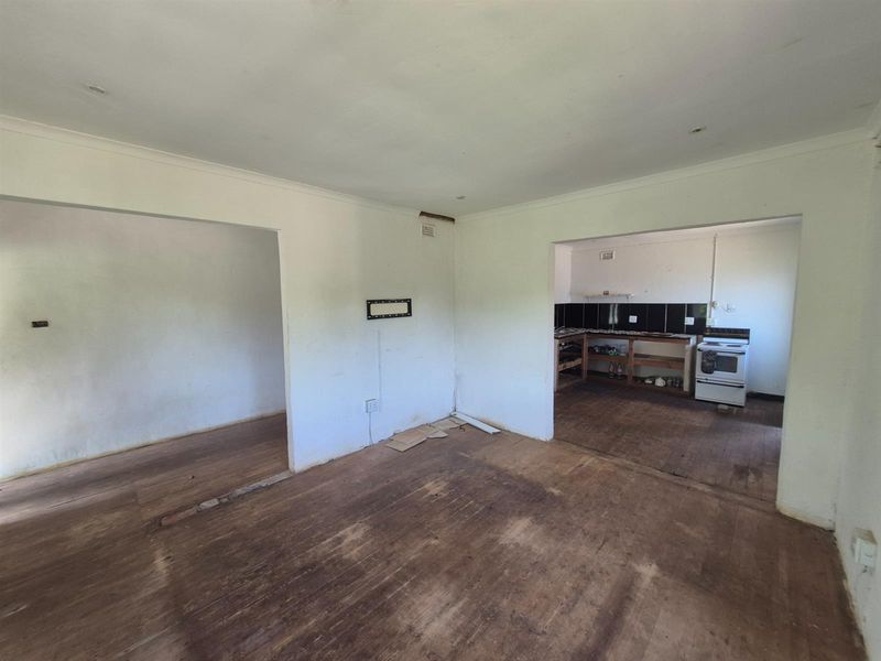 An open-plan living and kitchen area featuring original timber flooring, basic kitchen cabinetry, and a freestanding stove, requiring significant renovation and cosmetic updates.