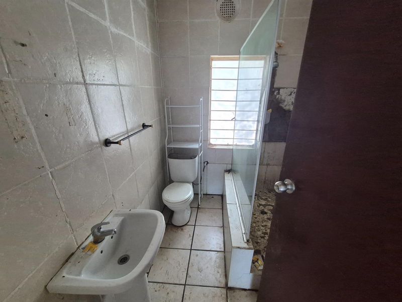 A dated bathroom featuring a pedestal basin, toilet, and a shower enclosure with visible wear to the wall and floor finishes.
