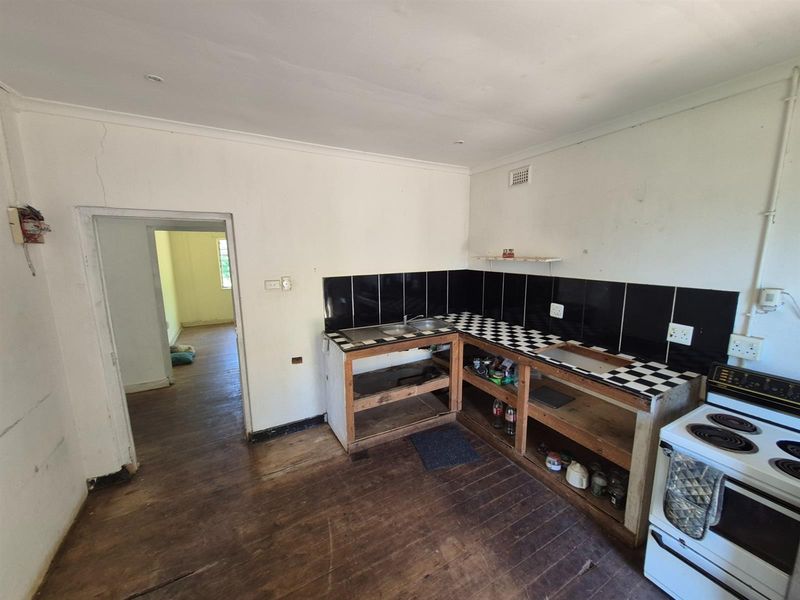 A dated kitchen area featuring open-frame cabinetry, a tiled countertop, and a freestanding electric stove, requiring significant renovation and cosmetic updates.