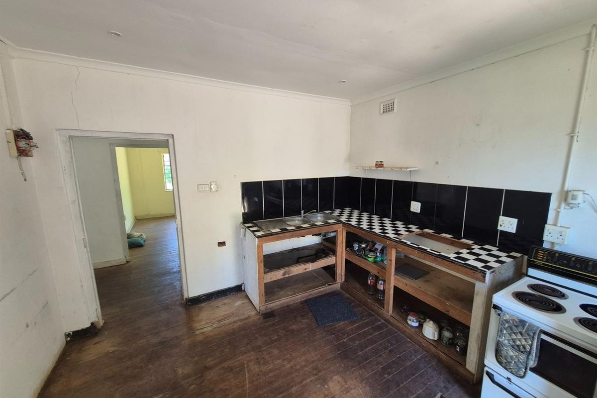 A dated kitchen area featuring open-frame cabinetry, a tiled countertop, and a freestanding electric stove, requiring significant renovation and cosmetic updates.