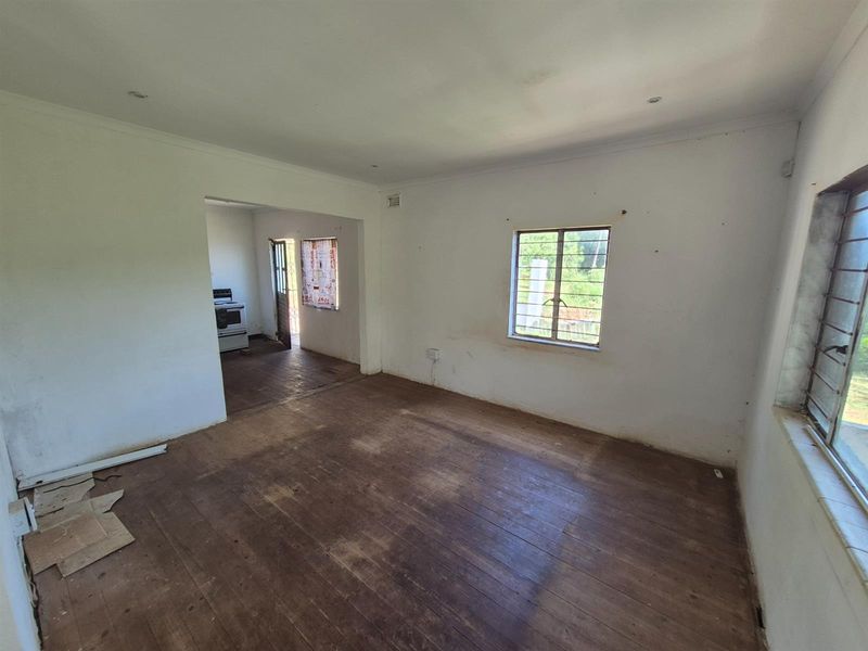 An empty living area featuring original timber flooring and large windows, with an open-plan transition leading into the kitchen space.