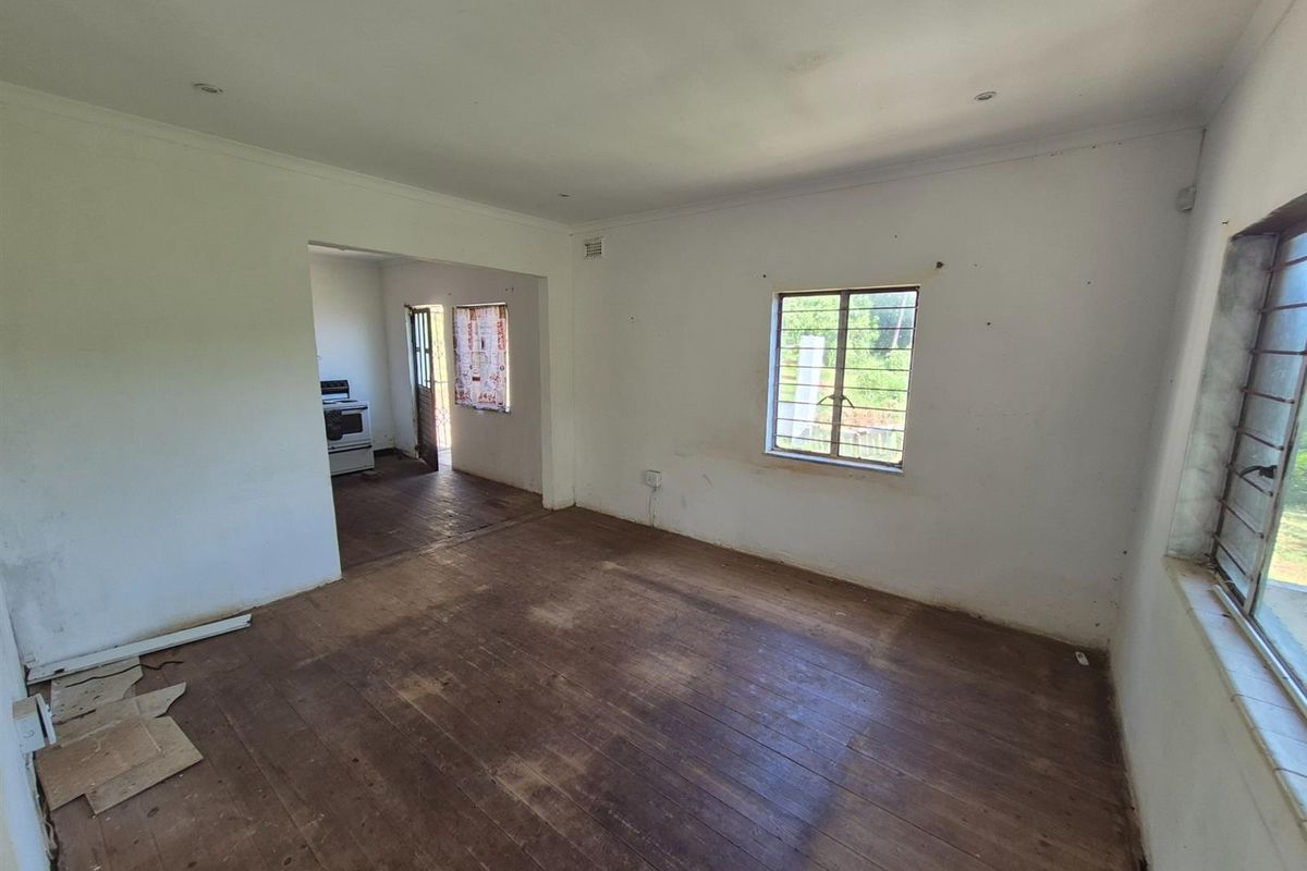 An empty living area featuring original timber flooring and large windows, with an open-plan transition leading into the kitchen space.