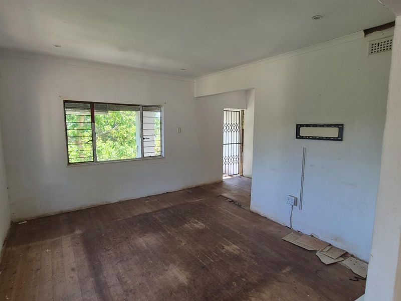 An empty living room featuring original timber flooring, large window, and direct access to an exterior security gate.