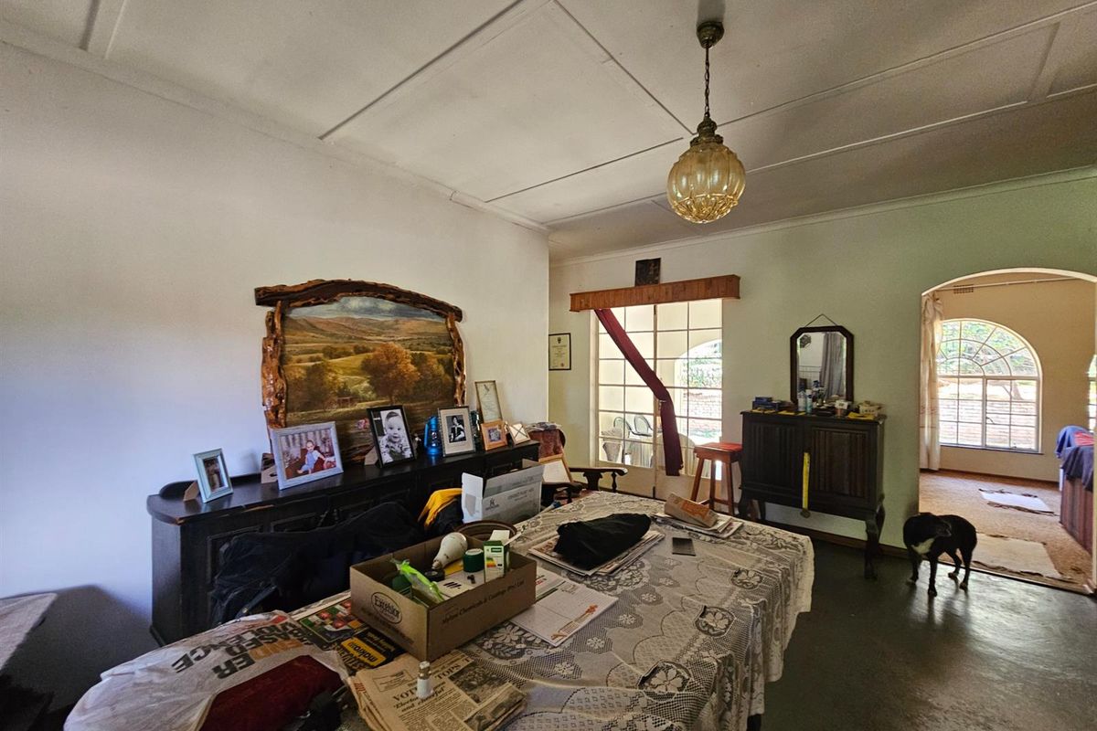 A living area featuring a classic pendant light fixture, arched doorway, and large windows providing natural light, with access to an adjacent room.