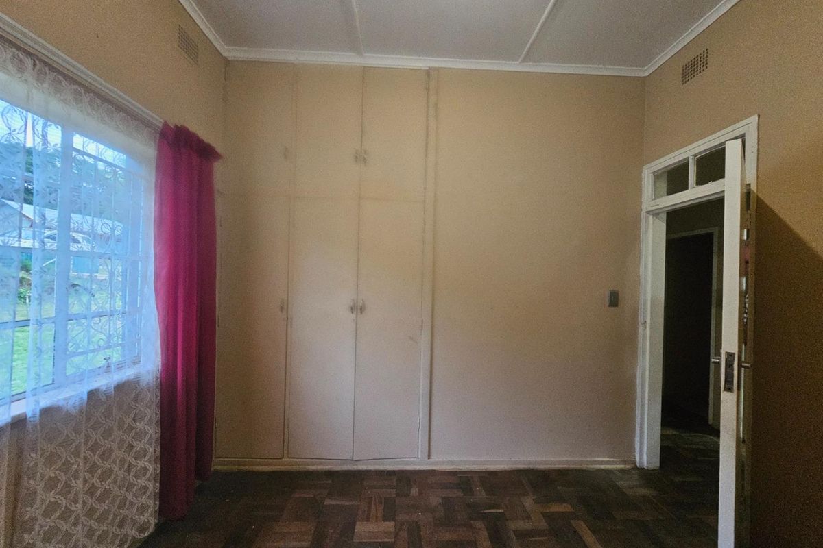 A bedroom featuring original parquet flooring, built-in storage cupboards, and a window with security bars.