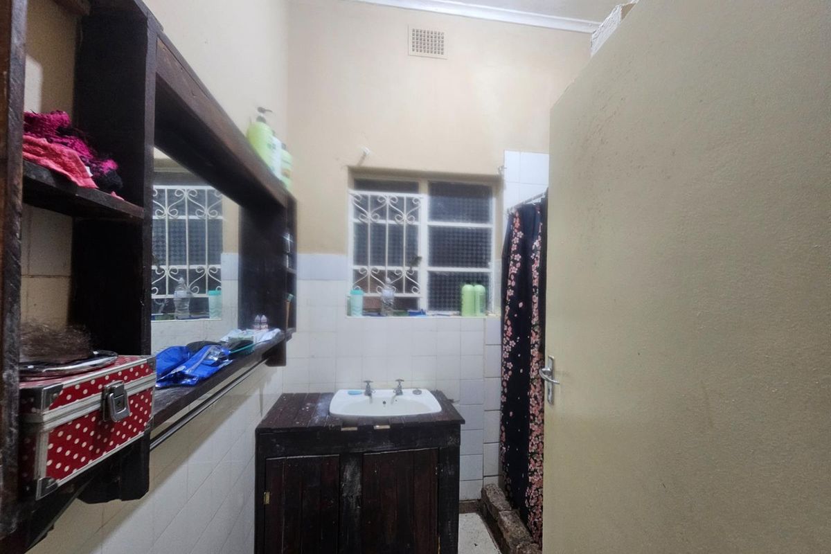 A functional bathroom featuring a vanity basin, tiled splashback, and shower area with security bars on the window.