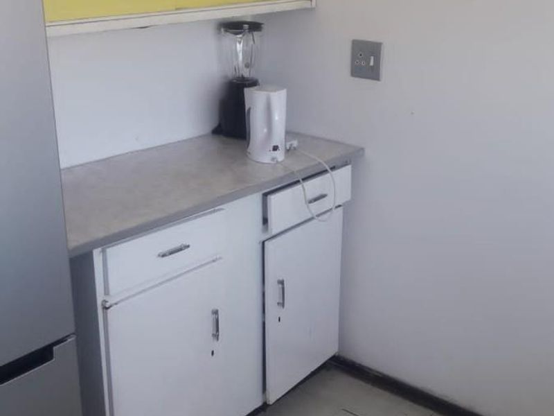 A small kitchen area featuring basic built-in cabinetry, laminate countertops, and damaged floor tiling in need of repair or replacement.