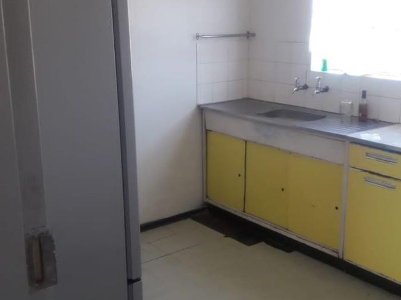 A functional kitchen space featuring built-in cabinetry, a stainless steel sink, and tiled splashbacks, offering potential for modernization and renovation.
