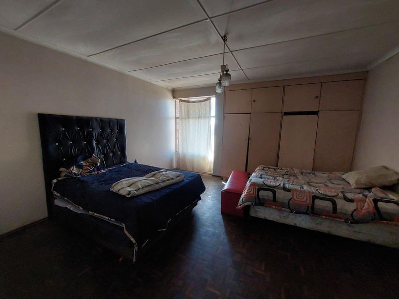 Spacious bedroom featuring built-in cupboards, parquet flooring, and a tiled ceiling, offering a functional layout with potential for modernization.