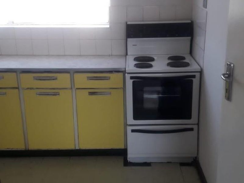 A functional kitchen space featuring yellow built-in cabinetry, a laminate countertop, and a freestanding electric stove with a tiled splashback.