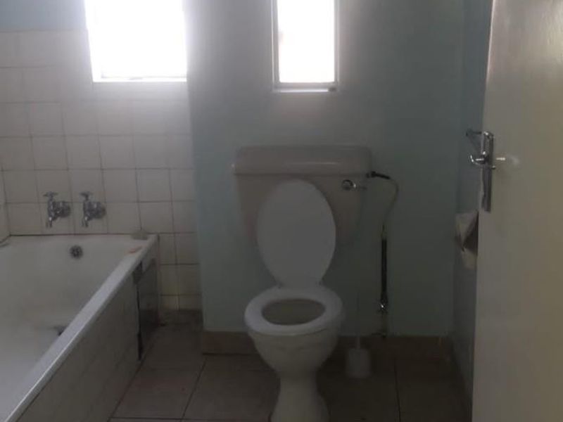 A functional bathroom featuring a standard bathtub, toilet, and tiled finishes, offering a blank canvas for potential modernization and renovation.