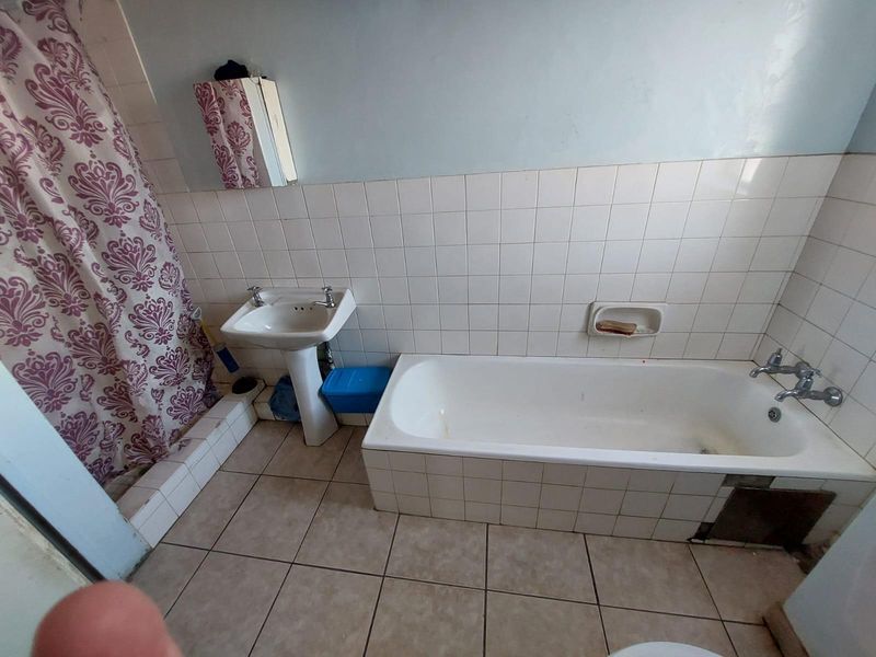 A dated bathroom featuring a pedestal basin, built-in bathtub with tiled surround, and ceramic wall and floor tiling.