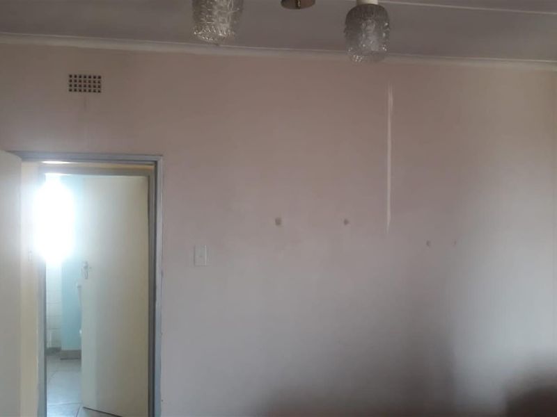 An empty bedroom featuring a ceiling light fixture, ventilation grille, and an internal door leading to an adjacent room.