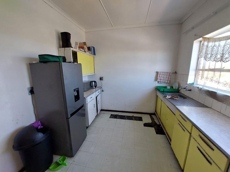 A dated kitchen featuring original yellow cabinetry, a stainless steel sink, and damaged floor tiles, offering significant potential for a modern renovation.