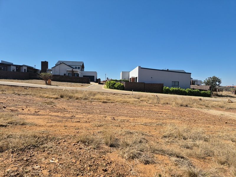 A view of a vacant residential plot situated in a developed estate with paved road access and surrounding modern homes.