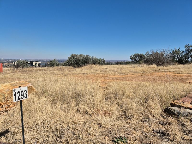 A view of a vacant residential plot featuring natural dry grass and surrounding landscape, suitable for future development.
