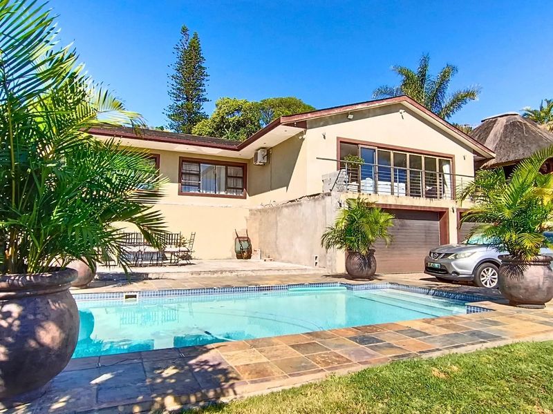 Rear exterior view of the house featuring a swimming pool, paved patio area, balcony, and integrated garage.