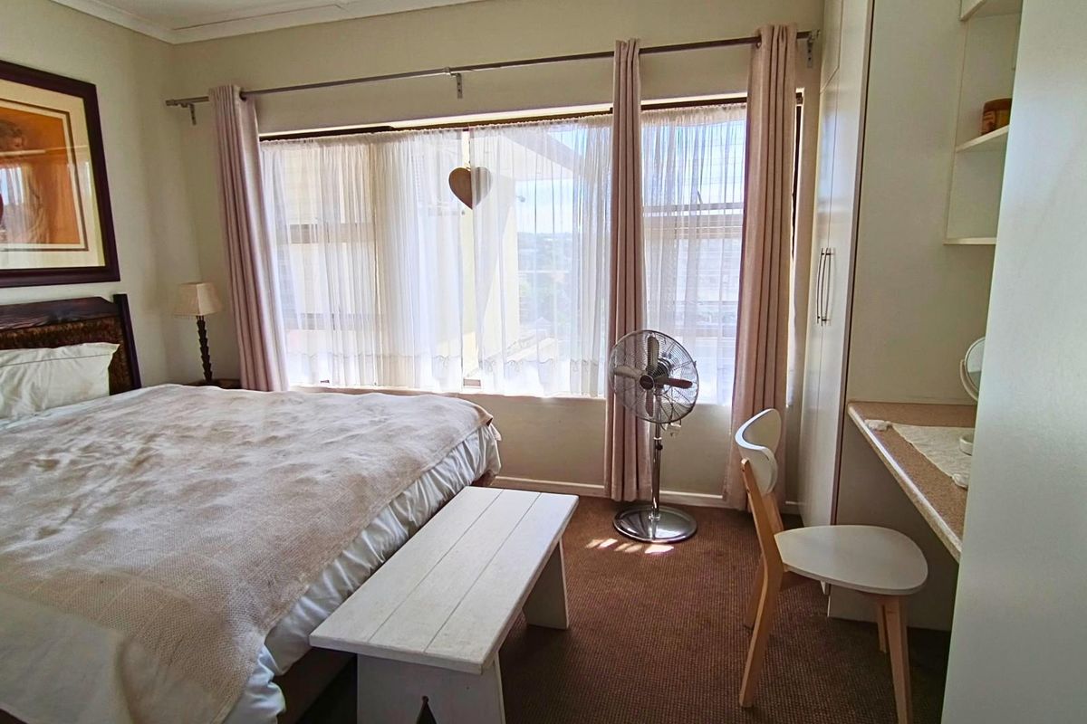 A bedroom featuring built-in cupboards, a built-in desk area, and large windows with curtain rails, providing natural light.