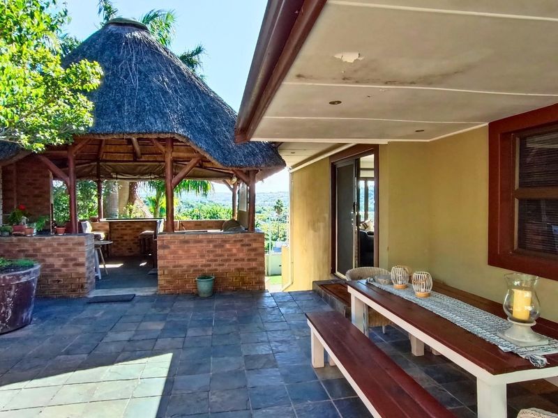 Covered patio area featuring tiled flooring, recessed lighting, and an adjacent thatched lapa with a built-in brick braai, ideal for outdoor entertaining.