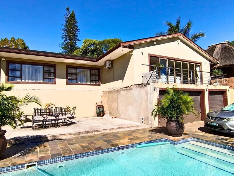 Rear exterior view featuring a swimming pool, paved patio area, elevated balcony, and double garage access.