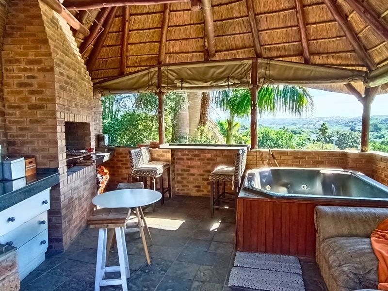 Covered outdoor entertainment area featuring a thatched roof, built-in brick braai, granite prep surfaces, and a built-in spa bath with scenic views.