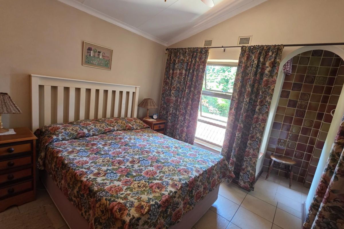 A bedroom featuring a vaulted ceiling, tiled flooring, and an arched entryway leading to an en-suite bathroom area with vintage-style wall tiling.