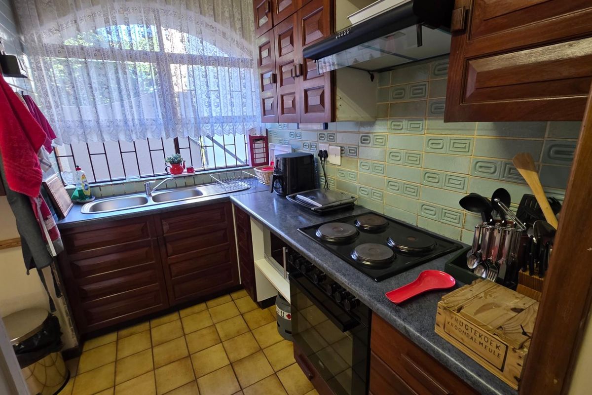A functional kitchen featuring dark wood cabinetry, a built-in electric hob and oven, double sink, and tiled backsplash.