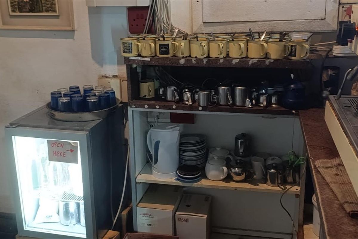 A functional restaurant beverage preparation area featuring a commercial espresso machine, under-counter refrigeration, and open shelving for service equipment.