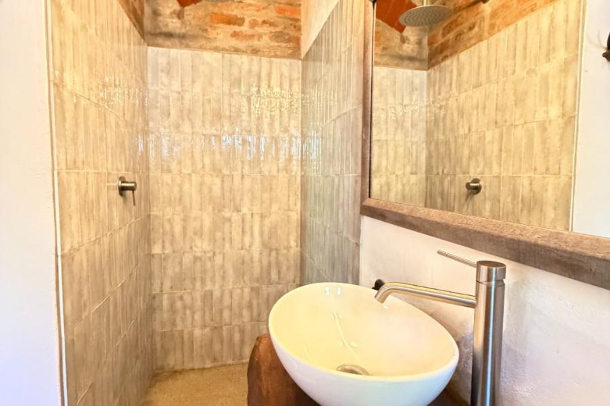 A modern bathroom featuring a walk-in shower with exposed brickwork, tiled walls, a vessel sink on a wooden vanity, and a large wall mirror.