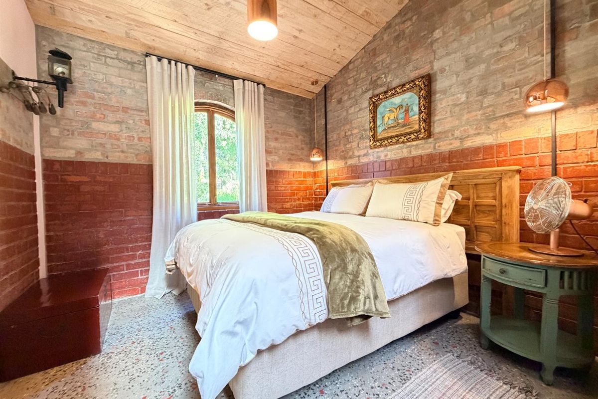 A rustic bedroom featuring exposed brick walls, a vaulted timber ceiling, and polished terrazzo flooring, creating a warm and character-filled living space.