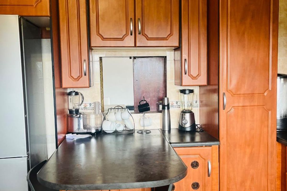 A kitchen area featuring traditional wood-finish cabinetry, dark laminate countertops, and tiled splashbacks, providing functional storage and workspace.