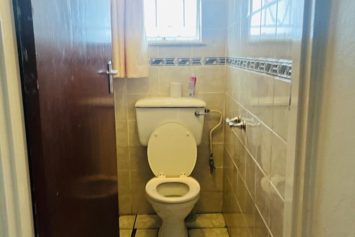 A compact bathroom featuring a standard toilet, tiled walls with a decorative border, and tiled flooring.