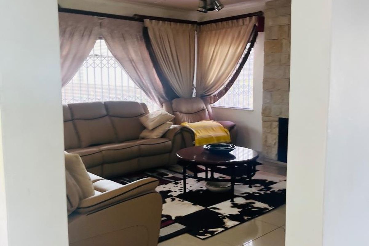 A comfortable living room featuring tiled flooring, a stone-clad fireplace, and a ceiling fan, viewed through an arched doorway.