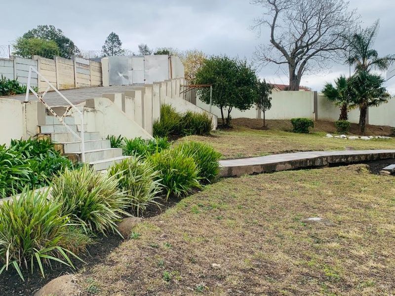 Rear garden area featuring concrete retaining walls, a set of stairs, and established landscaping with a paved walkway.