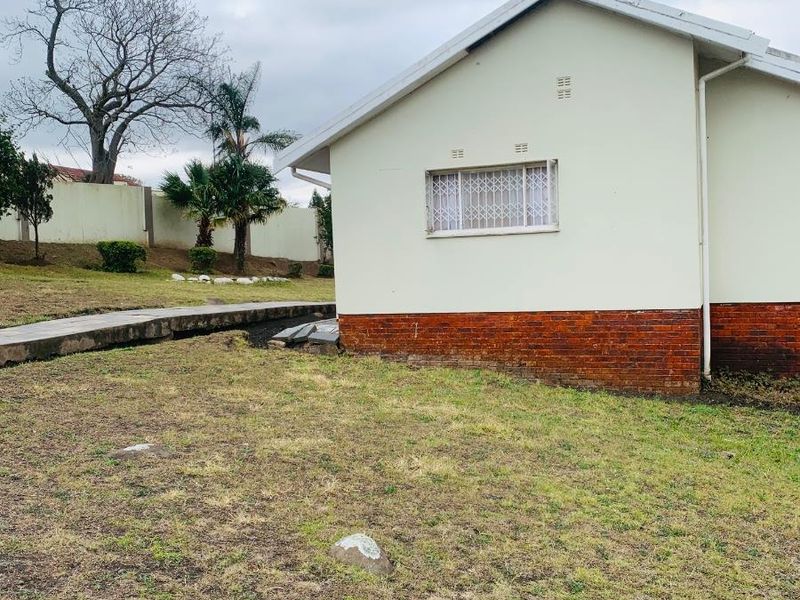 Side view of the house exterior featuring a brick base, painted walls, and security bars on the window, set within a large garden area.