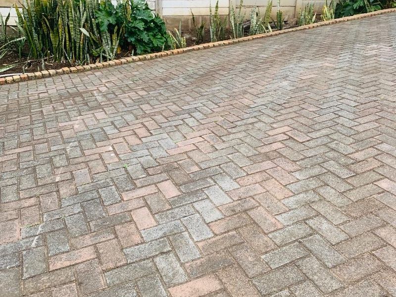 A paved driveway area featuring herringbone brickwork and a perimeter boundary wall with established garden border planting.