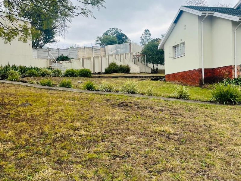 A view of the rear garden area featuring a sloped lawn, retaining walls, and the side elevation of the house.